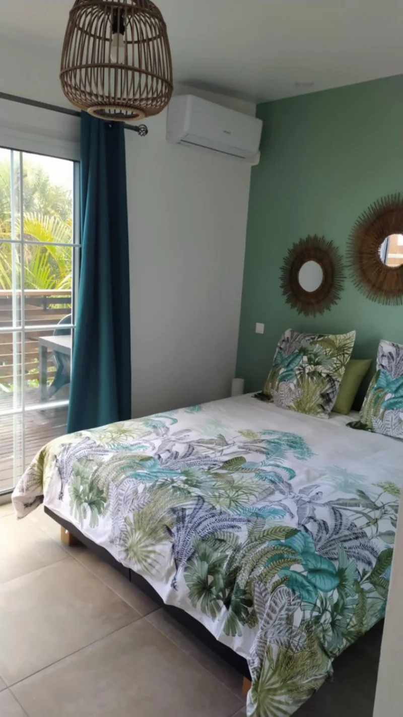 Le lit de la chambre Paille-en-queue, sa housse à feuillage tropical et la baie vitrée