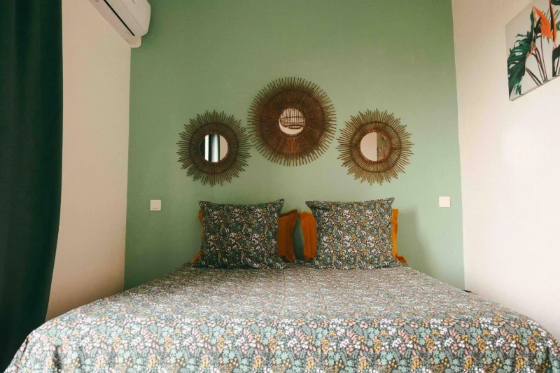 Une chambre aux murs vert d'eau, avec ses miroirs soleil au-dessus du lit